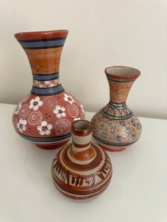 three vases sitting on top of a white table next to each other and one has flowers painted on it