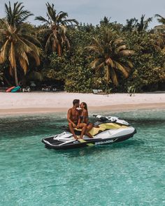 two people sitting on the back of a jet ski in clear blue water with palm trees behind them