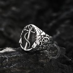 a silver ring with an anchor and wheel on it sitting on top of a rock