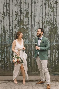 a man and woman standing next to each other in front of a wooden wall with peeling paint