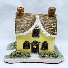 a small yellow house with two chimneys and a light at the top on a white surface