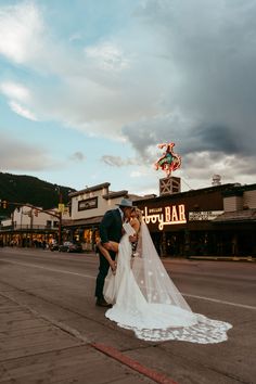 a bride and groom kissing on the street in front of an old fashioned neon sign