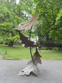 a metal sculpture in the middle of a park with leaves on it's sides