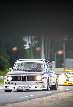 two cars driving on a race track with trees in the backgrouffs