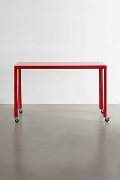 a red table sitting on top of a hard wood floor next to a white wall