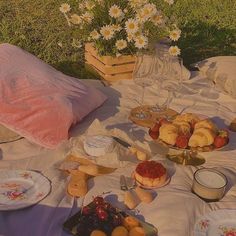 an outdoor picnic with bread, fruit and pastries on a blanket in the sun