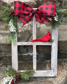 a red cardinal sitting on top of a window sill decorated with pine cones and greenery