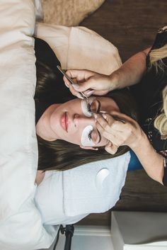 a woman is getting her hair done while another person uses a cell phone on the bed