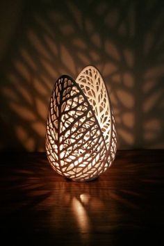 two white vases sitting on top of a wooden table next to a shadow cast wall