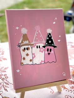 a pink canvas with two ghostes on it sitting on a table next to a teddy bear