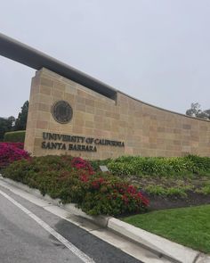 the university of california santa barbara sign is in front of some bushes and flowers on either side of the road