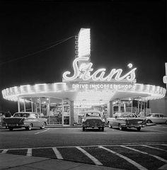 an old gas station with cars parked in the lot and neon signs on the building