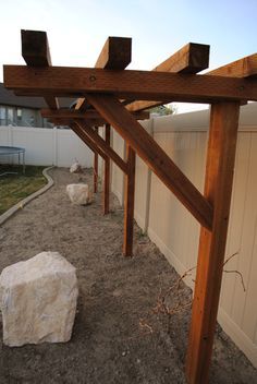 a wooden pergolan in the middle of a yard next to a fence and building