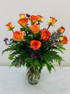 a vase filled with lots of orange roses on top of a white countertop next to a wall