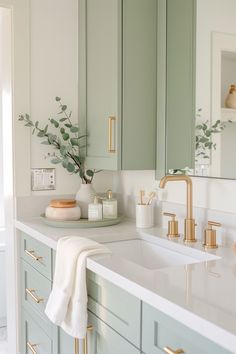 a bathroom with green cabinets and gold faucets on the countertop, along with a white towel