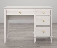 a white desk with two drawers and gold knobs on the top, in an empty room