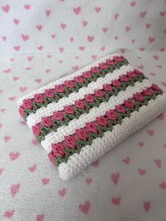 a crocheted wallet sitting on top of a pink and green blanket covered in hearts