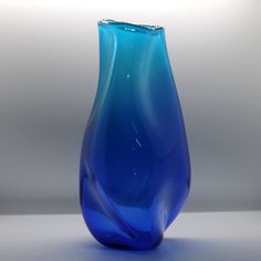 a blue glass vase sitting on top of a white table next to a gray wall