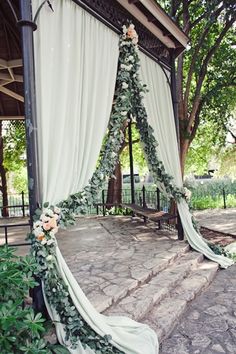 an outdoor wedding ceremony setup with white drapes and greenery on the side, along with flowers