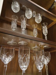 many wine glasses are lined up on the shelf in front of some other glassware