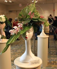 a white mannequin head with flowers on it in a room full of people