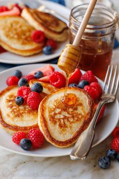 pancakes with syrup being poured onto them and topped with berries