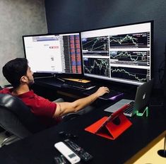 a man sitting at a desk in front of two computer monitors with graphs on them