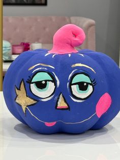 a blue pumpkin with eyes and stars painted on it's face, sitting on a table