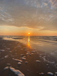 the sun is setting at the beach with footprints in the sand and water on the shore