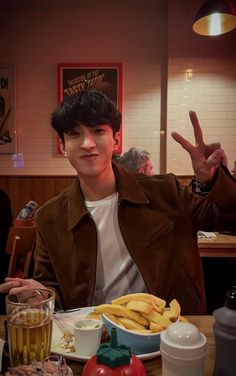 a man sitting at a table with food in front of him and making the peace sign