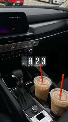 two iced coffees are sitting in the center console of a car with an alarm clock