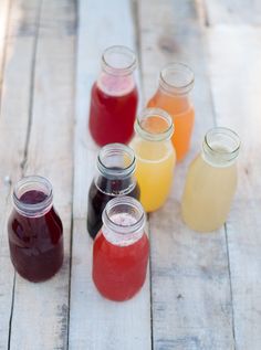 several jars filled with different colored liquid on top of a wooden table next to each other