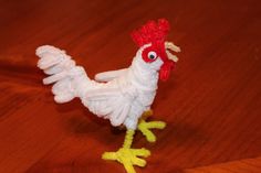 a small white and red chicken sitting on top of a wooden table