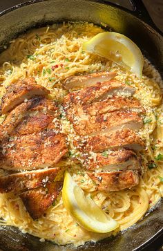 some meat and noodles in a skillet with lemon wedges on the side for garnish