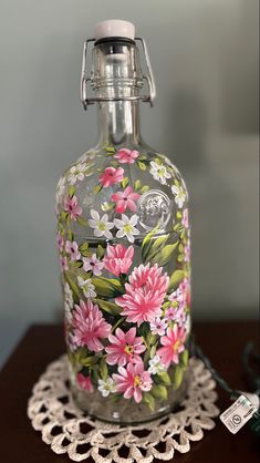 a glass bottle with flowers painted on it sitting on a doily next to a wall