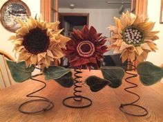 three sunflowers sitting on top of a wooden table next to metal spiral wire