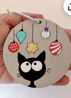 a hand holding a round ornament with a black cat on it