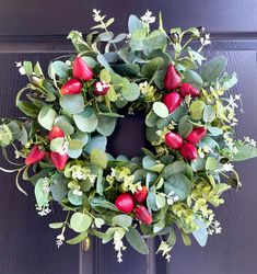 a wreath with strawberries and greenery hanging on a door