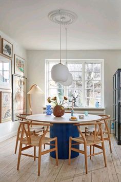 a dining room table and chairs with artwork on the wall behind it in front of a window