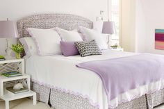 a bed with white sheets and purple pillows