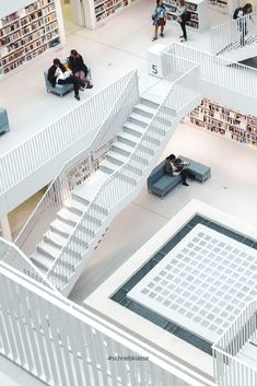 people are sitting on benches and reading books in a large room with stairs leading up to the second floor