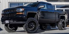 a black truck is parked in front of a building with large tires on it's rims