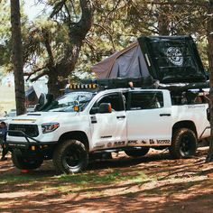 a white truck parked in the woods with a tent attached to it's back