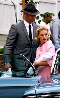 a man and woman standing next to a blue car