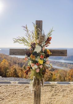 a cross decorated with flowers and greenery on top of a hill in the fall