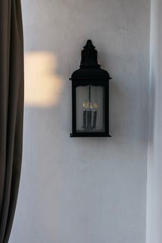 an old fashioned wall light hanging on the side of a white building with three candles in it