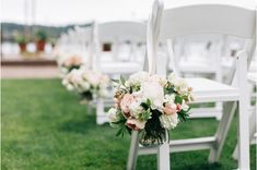 white chairs lined up in the grass with pink and white flowers on each one side