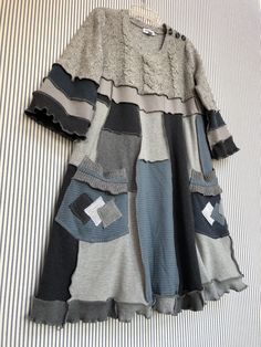 a dress that is laying on top of a striped bed sheet with buttons and holes in it