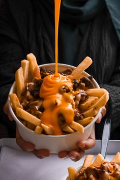 someone is pouring cheesy fries into a bowl