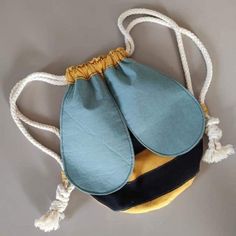 a blue and yellow handbag hanging from a rope on a gray wall with white cords